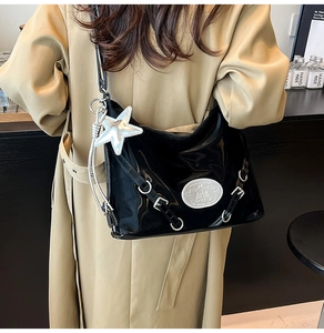 Detail of glossy black patent leather tote with star charm and silver buckles on model