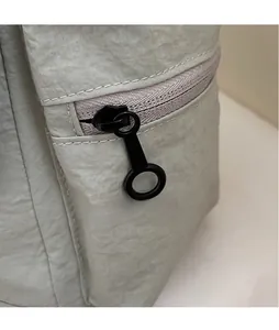 Detailed macro of smooth round metal zipper head on a light gray fabric shoulder bag
