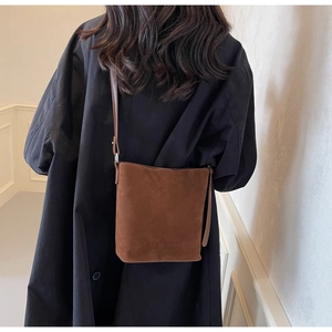 Close-up of brown frosted suede bucket bag featuring embossed text and slim strap