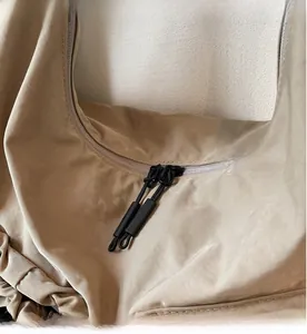 Dettaglio della doppia cerniera scorrevole con tiranti in corda su borsa in nylon beige