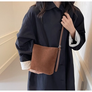 Detail of a brown suede bucket bag with FASHION & BAGS embossing and a long shoulder strap