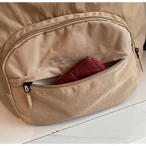 Close-up of front zipper pocket on beige nylon backpack showing storage for a wallet