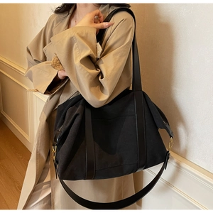 Detail of black canvas tote bag showing wide leather straps and gold metal hooks