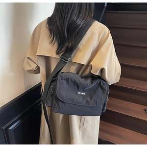 Close-up of a black nylon crossbody messenger bag worn by a model in casual street style