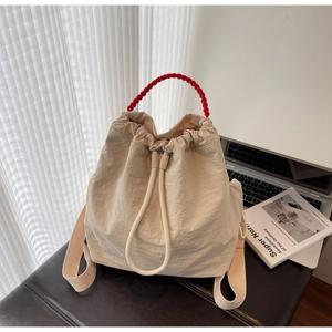 Dettaglio borsa a secchiello in nylon beige con manico rosso intrecciato e chiusura a coulisse
