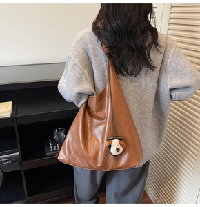 Detail view of large brown soft leather hobo bag with a cute beige plush puppy charm
