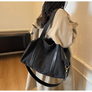 Detail of black canvas tote bag with adjustable shoulder strap worn by model in a room