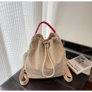 Dettaglio della borsa a secchiello beige con coulisse e manico intrecciato rosso a contrasto
