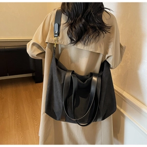 Black large capacity canvas tote bag worn over the shoulder with a beige trench coat