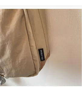 Dettaglio macro della borsa in nylon kaki con etichetta nera del logo e cuciture rifinite