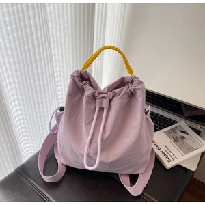 Dettaglio borsa a secchiello in nylon lilla con manico intrecciato giallo su sgabello