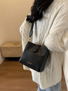 Sac seau rétro noir avec texture plissée et large bandoulière rayée porté par un mannequin