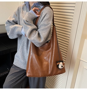 Brown faux leather tote bag detail with plush dog pendant and natural textured finish