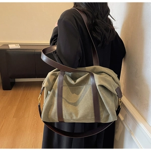 Detail view of large olive green canvas tote bag with brown leather handles and gold buckles