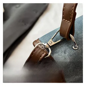 Detail of blue denim fabric with brown leather trim and silver metal hook on backpack