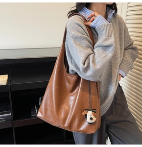 Detailed view of brown hobo tote bag with lychee texture and cute plush dog charm accessory