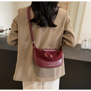Close-up of a burgundy half-moon saddle bag with suede and leather patchwork detail