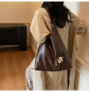 Detail view of a large brown faux leather tote bag with a cute plush dog charm accessory