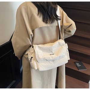 Detail of cream nylon crossbody bag with crinkled texture on a wooden staircase