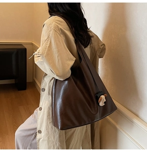 Deep brown oversized tote bag with plush puppy charm shown on model shoulder