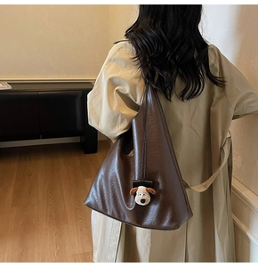 Brown faux leather tote bag with dog pendant shown on shoulder in a minimalist room