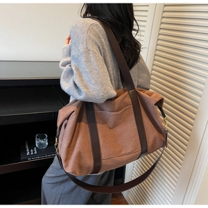 Detail of brown canvas tote bag featuring premium leather handles and gold metal buckles