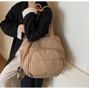 Detail view of a beige nylon tote bag featuring front zip pocket and side elastic pocket