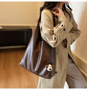 Detail of vintage brown tote bag with plush dog charm worn by a model in a beige coat