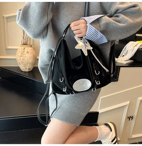 Detail of black glossy shoulder bag with silver hardware and star charm on a model