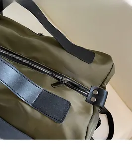 Close-up of military green nylon fabric with premium metal zipper and leather strap detail