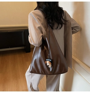 Detail of dark brown large tote bag with leather texture and cute plush puppy charm