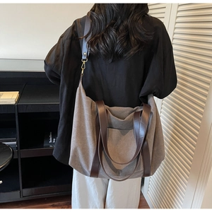 Grey canvas tote bag with brown leather handles shown worn over the shoulder in a study