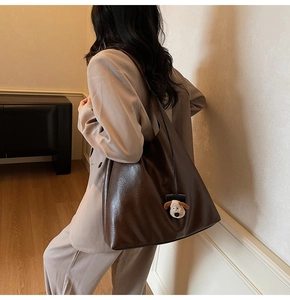 Detail of dark brown leather hobo bag with a cute plush dog charm on the shoulder strap