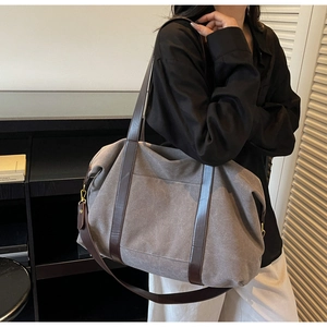 Detail view of a large taupe canvas travel bag with brown leather handles and side buckles
