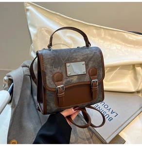 Detail of vintage gray denim backpack with brown faux leather trim and silver metal plaque