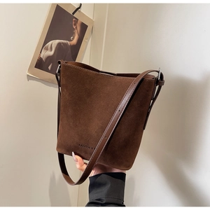 Detail showing the dark brown suede bucket bag texture and adjustable strap buckle