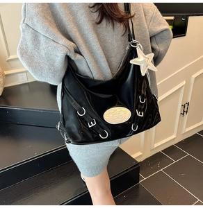 Close-up of black glossy patent leather hobo bag with silver star charm and metal plate