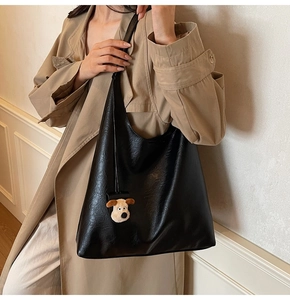 Large black shoulder bag with leather texture and cute cartoon puppy charm on a trench coat