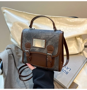 Detail view of denim and brown leather satchel with metal buckle and logo plate