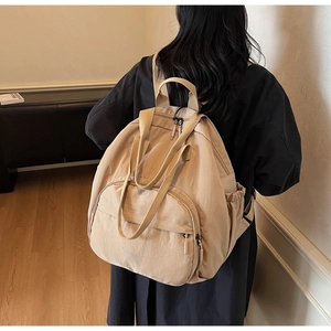 Detail showing the beige nylon backpack with side pockets and main zipper compartment