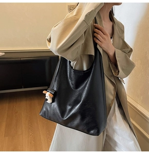 Large black leather tote bag with a cute puppy plush charm accessory on the shoulder strap