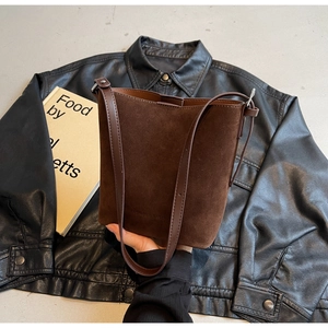 Detail of brown suede bucket bag with leather stitching and debossed fashion logo
