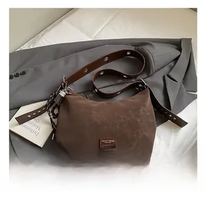 Detail of a brown matte crescent bag with a wide eyelet strap on a grey blazer background