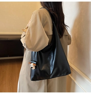 Large black leather tote bag with cute dog charm shown on a beige trench coat