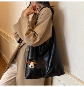 Detail of black tote bag with lychee texture and cute plush puppy charm on beige trench coat