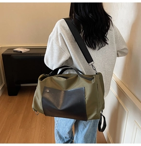 Close-up of olive green travel bag showing black leather pockets and wide shoulder strap
