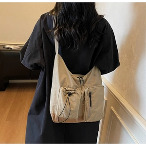 Dettaglio borsa a tracolla kaki con multitasche e coulisse su cappotto nero lungo