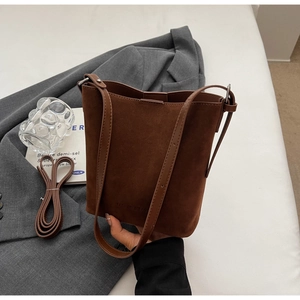 Detail of dark brown suede bucket bag with embossed logo and adjustable leather strap