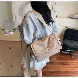 Close-up of a khaki canvas messenger bag with a wide strap shown on a female model