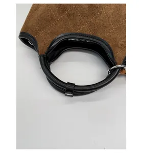 Détail du sac seau en daim montrant la texture matelassée, les poignées en cuir et le métal